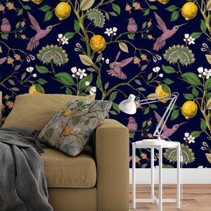 May include: A brown couch with a gray throw blanket and a patterned pillow sits in front of a wall with a dark blue background and a repeating pattern of lemons, flowers, and hummingbirds.