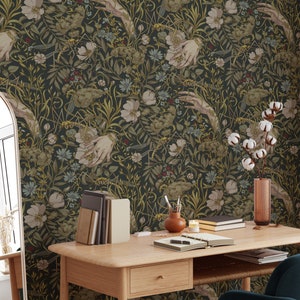 Puede incluir: Papel pintado floral oscuro con un patr&oacute;n repetido de manos, flores y follaje en tonos verdes, beige y dorados. El papel pintado est&aacute; en una pared detr&aacute;s de un escritorio de madera con libros, un jarr&oacute;n y una silla.