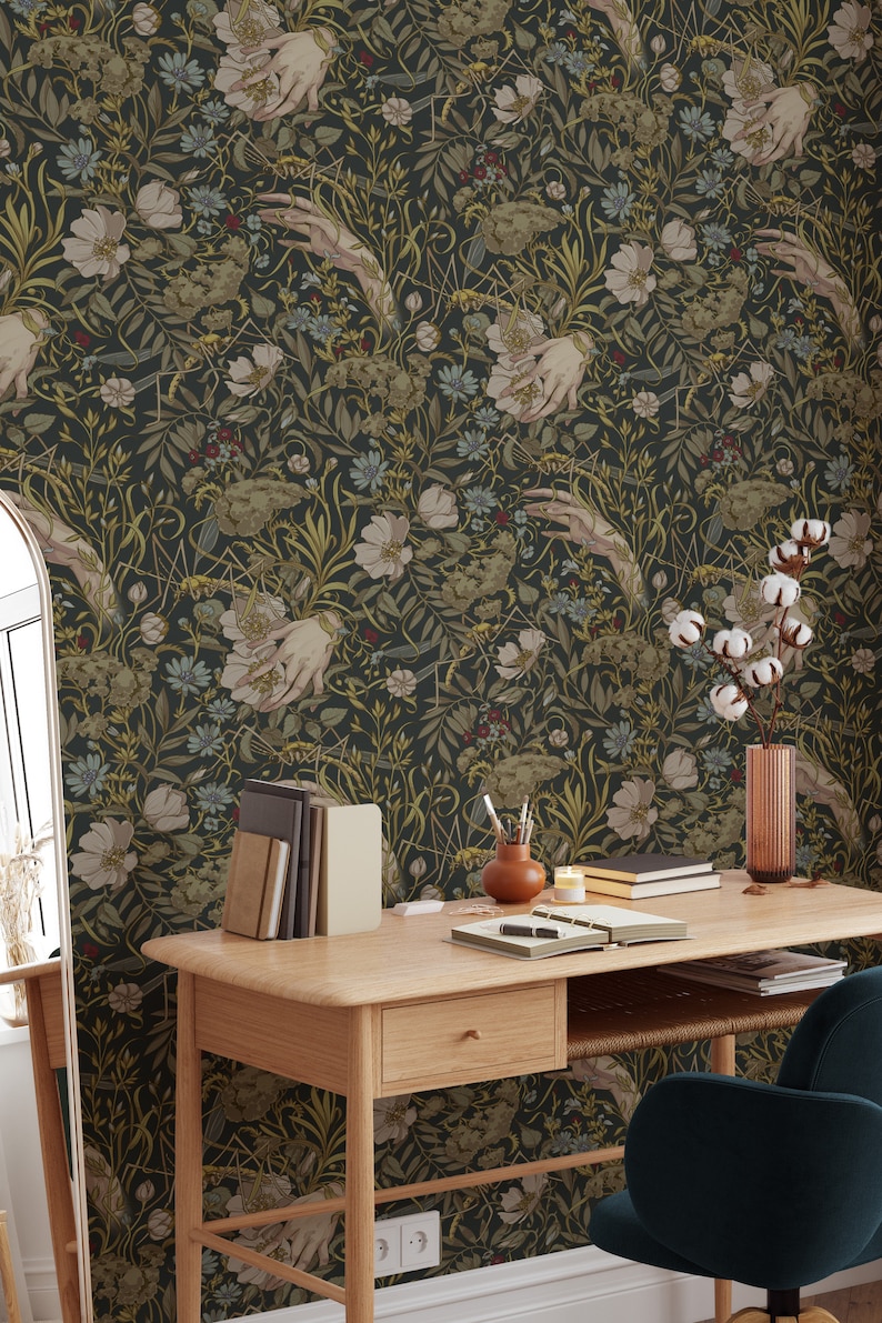 Puede incluir: Papel pintado floral oscuro con un patr&oacute;n repetido de manos, flores y follaje en tonos verdes, beige y dorados. El papel pintado est&aacute; en una pared detr&aacute;s de un escritorio de madera con libros, un jarr&oacute;n y una silla.