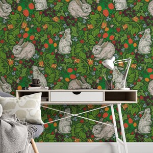 Op de afbeelding: Een groene behang met een herhalend patroon van witte konijnen en rode en oranje bessen. Het behang is achter een wit bureau met een lade en een witte lamp.