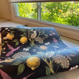 May include: A roll of black wallpaper with a floral pattern featuring lemons, leaves, and hummingbirds. The wallpaper has a dark background with colorful accents.