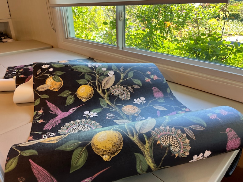 May include: A roll of black wallpaper with a floral pattern featuring lemons, leaves, and hummingbirds. The wallpaper has a dark background with colorful accents.
