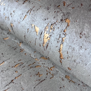 Può includere: Primo piano di una carta da parati in sughero grigia e marrone con una superficie testurizzata. La carta da parati ha un aspetto metallico e una sottile lucentezza dorata.