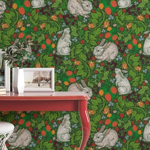 Op de afbeelding: Groene behang met een herhalend patroon van witte konijnen en rode bessen. De behang is te zien in een kamer met een rode tafel en een witte kruk.