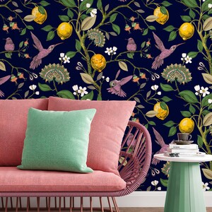 May include: A pink couch with a green pillow sits in front of a dark blue wall with a floral pattern. The pattern features hummingbirds, lemons, and flowers.