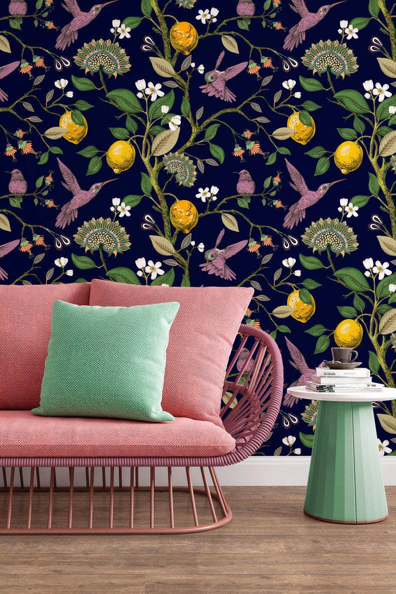May include: A pink couch with a green pillow sits in front of a dark blue wall with a floral pattern. The pattern features hummingbirds, lemons, and flowers.