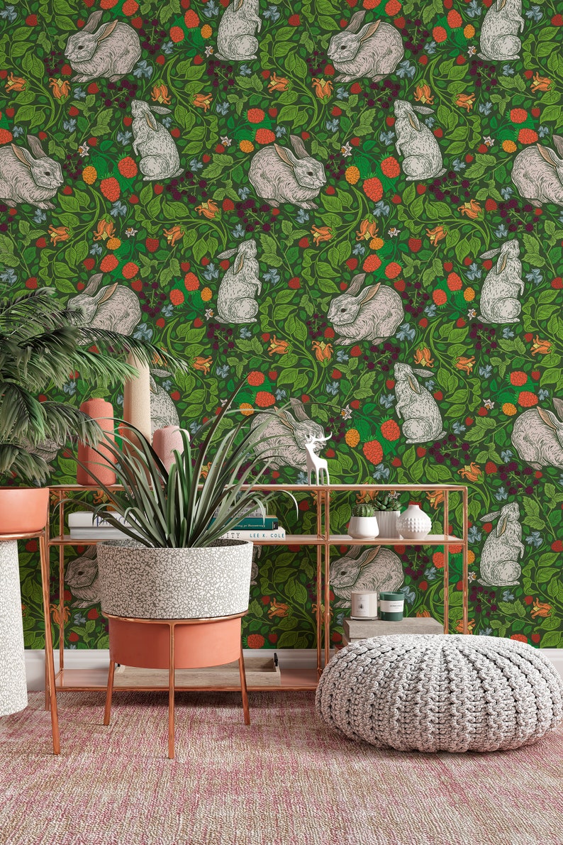 Op de afbeelding: Een groene behang met een herhalend patroon van witte konijnen en rode bessen. De behang is achter een plank met een potplant en een decoratieve voetenbank.