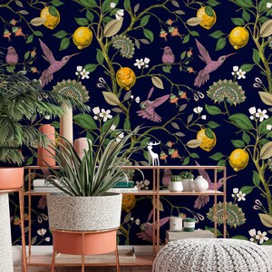 May include: A navy blue wallpaper with a repeating pattern of lemon trees, hummingbirds, and white flowers. The wallpaper is displayed in a room with a potted plant, a shelf, and a decorative footstool.