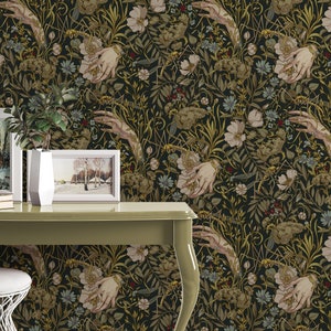 Puede incluir: Papel pintado oscuro con un patr&oacute;n repetido de manos, flores y follaje en tonos verdes, beige y dorados. El dise&ntilde;o presenta manos estilizadas sosteniendo arreglos florales sobre un fondo negro. El papel pintado est&aacute; instalado en una pared.