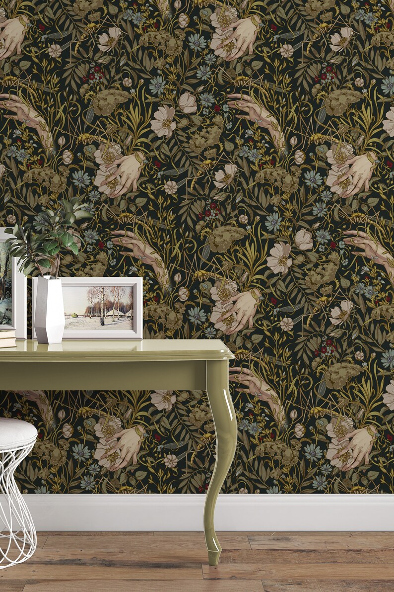 Puede incluir: Papel pintado oscuro con un patr&oacute;n repetido de manos, flores y follaje en tonos verdes, beige y dorados. El dise&ntilde;o presenta manos estilizadas sosteniendo arreglos florales sobre un fondo negro. El papel pintado est&aacute; instalado en una pared.