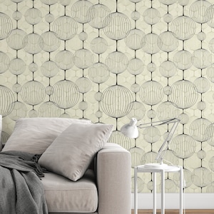 以下が含まれることがあります： ベージュのソファに灰色の毛布がかけられており、白いサイドテーブルにはランプが置かれています。 ソファの後ろの壁は、黒い円形の模様がついた幾何学模様の壁紙で覆われています。