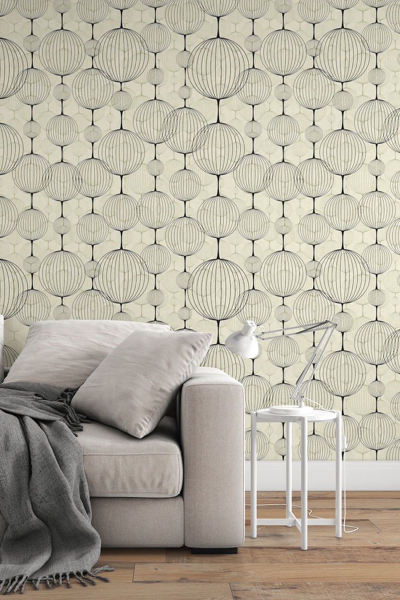 以下が含まれることがあります： ベージュのソファに灰色の毛布がかけられており、白いサイドテーブルにはランプが置かれています。 ソファの後ろの壁は、黒い円形の模様がついた幾何学模様の壁紙で覆われています。