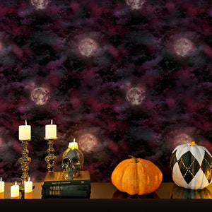 Może przedstawiać: Scena halloweenowa z czarną, białą i złotą dynią, pomarańczową dynią, czaszką i świecami na ciemnym stole przed ciemnym fioletowym i czarnym tłem z białymi księżycami i gwiazdami.