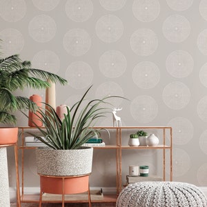 May include: A gray wall with a white dot pattern, a potted plant on a gold metal shelf, a gray knitted pouf on a pink rug, and a white deer figurine on the shelf.