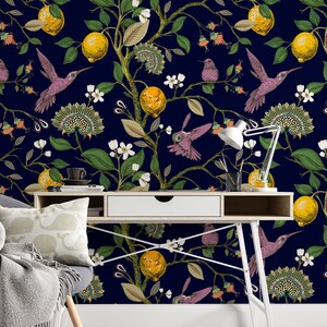 May include: A white desk with a drawer and a white lamp sits in front of a dark blue wall with a floral wallpaper pattern. The wallpaper features hummingbirds, lemons, and flowers.