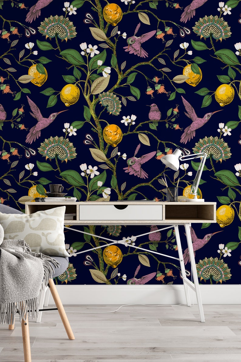 May include: A white desk with a drawer and a white lamp sits in front of a dark blue wall with a floral wallpaper pattern. The wallpaper features hummingbirds, lemons, and flowers.