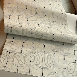 以下が含まれることがあります： 黒い幾何学的な円が繰り返しパターンで描かれた白い壁紙のロール。円は黒で縁取られており、内部にグリッド状のパターンがあります。