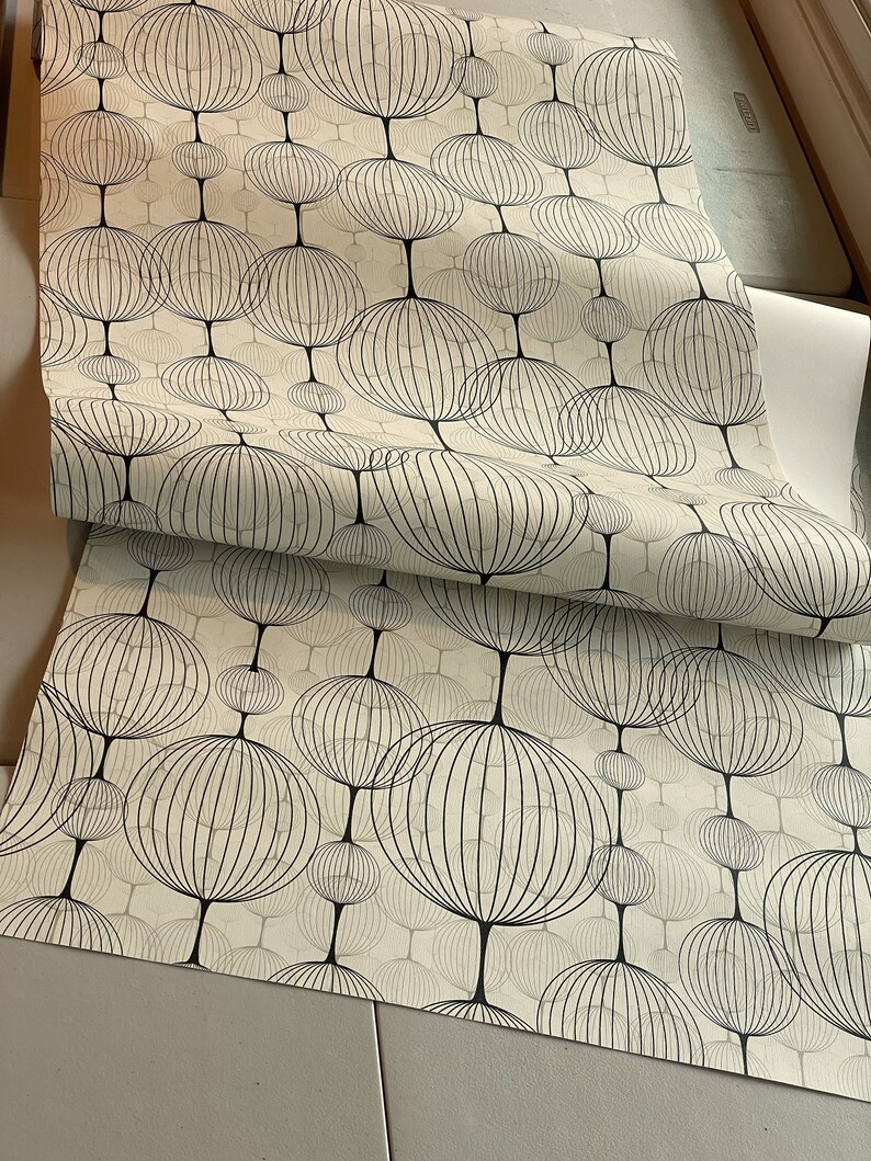 以下が含まれることがあります： 黒い幾何学的な円が繰り返しパターンで描かれた白い壁紙のロール。円は黒で縁取られており、内部にグリッド状のパターンがあります。