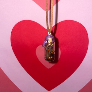 May include: A brown leather cord necklace with a small glass vial pendant filled with colorful glitter and a purple figurine.