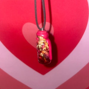 May include: A red glass bottle filled with dried flowers and herbs, sealed with red wax, hangs from a black cord necklace.