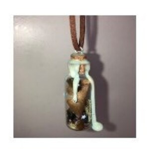 May include: A small glass bottle with a cork stopper filled with glitter, small stones, and a brown feather. The bottle is hanging from a brown cord necklace. The bottle is covered in a white substance that looks like wax.