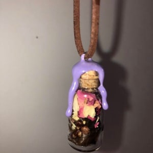 May include: A small glass bottle filled with dried flowers and herbs, sealed with a cork and topped with a purple wax seal. The bottle is attached to a brown cord, making it a necklace.