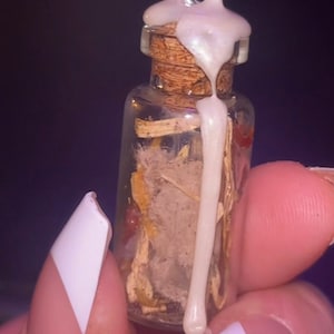May include: A small glass bottle with a cork stopper and a white wax seal. The bottle is filled with dried herbs and other natural materials.