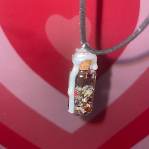 May include: A small glass bottle filled with dried herbs and flowers, sealed with a white wax and attached to a black cord necklace.