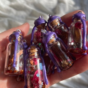 Peut inclure: Une collection de petites bouteilles en verre avec des gouttes de cire violette. Chaque bouteille contient des fleurs s&eacute;ch&eacute;es, des paillettes et des &eacute;toiles. Les bouteilles sont parfaites pour l'artisanat ou la d&eacute;coration.
