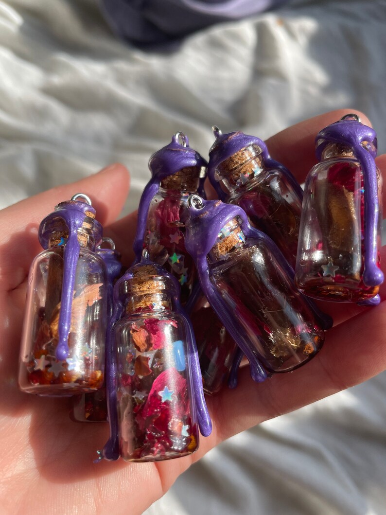 Peut inclure: Une collection de petites bouteilles en verre avec des gouttes de cire violette. Chaque bouteille contient des fleurs s&eacute;ch&eacute;es, des paillettes et des &eacute;toiles. Les bouteilles sont parfaites pour l'artisanat ou la d&eacute;coration.