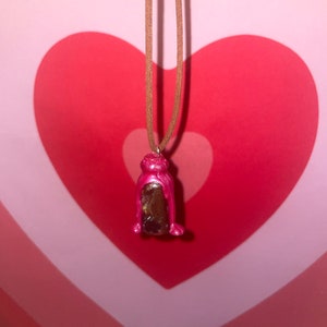 May include: A brown leather cord necklace with a pink and brown glass bottle pendant.