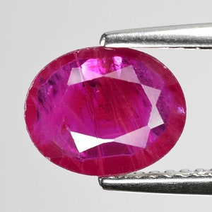 Pode incluir: Uma gema de rubi ovalada de cor rosa vibrante com corte facetado. O rubi é segurado por uma pinça.