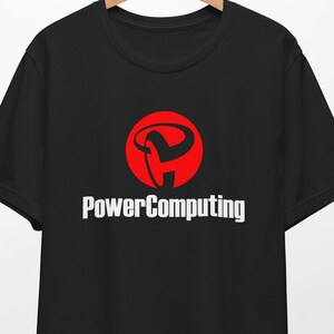 May include: Black t-shirt with a red and white logo. The logo features a stylized design inside a red circle, with the words "PowerComputing" in white below it. The shirt is hanging on a wooden hanger.