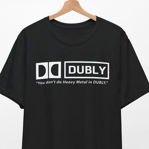 Puede incluir: Camiseta negra con un gráfico blanco que dice "DC DUBLY" y "You don't do Heavy Metal in DUBLY."