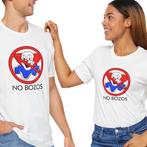 May include: Two white t-shirts with a red circle and a diagonal line through it. Inside the circle is a cartoon clown with a red nose and blue and red clothing. The text "NO BOZOS" is below the circle.