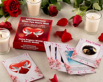 Könnte beinhalten: Ein Deck mit 52 Liebesorakelkarten in einer rosa und roten Schachtel mit einer weißen Taube und dem Text "Soul Connections When Two Hearts Meet Love Oracle Cards". Die Schachtel ist von roten Rosen und Kerzen umgeben.