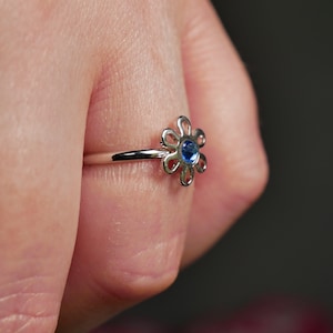 May include: A silver ring with a blue gemstone in the center, shaped like a flower.