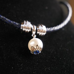 May include: A silver and blue necklace with a white pearl pendant. The necklace is made of braided leather and has a silver clasp.