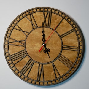 以下が含まれることがあります： ローマ数字の目盛りと黒と赤の時計と分針が付いた木製壁掛け時計。時計の文字盤は薄い茶色の木で、濃い茶色の木製の枠です。