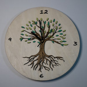 May include: A wooden clock with a tree design. The tree has green leaves and brown roots. The clock face has black numbers and hands. The clock is 12 inches in diameter.