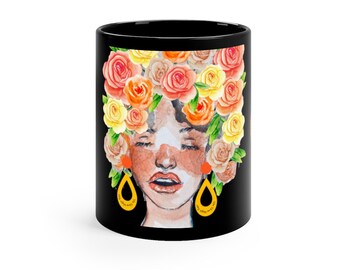 Puede incluir: Taza de café negra con una ilustración de acuarela de una persona con los ojos cerrados y una corona de flores naranja, amarilla y rosa. La persona lleva grandes pendientes amarillos en forma de lágrima.