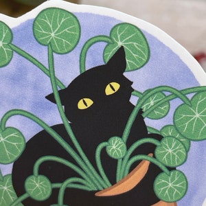 May include: A black cat with yellow eyes is nestled in a pot of green leafy plants. The cat is partially hidden by the leaves, with only its head and part of its body visible. The pot is brown and has a light blue background.