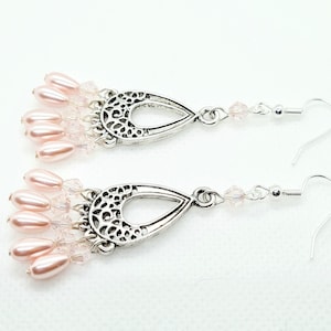 May include: A pair of dangle earrings with a silver filigree teardrop design. The earrings feature a cluster of pink pearl beads and clear crystal beads.