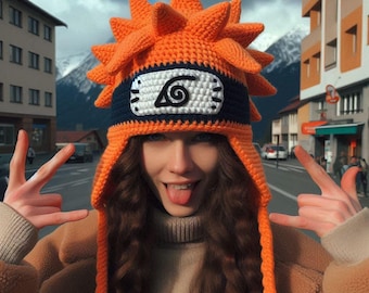 May include: A woman wearing a bright orange crocheted hat with a black and white symbol on the front. The hat has long orange tassels. The woman is smiling and sticking her tongue out.
