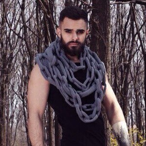 Może przedstawiać: Mężczyzna z brodą w czarnym tank topie i czarnych spodniach. Nosi szalik z łańcucha w kolorze szarym wokół szyi. Stoi w lesie.