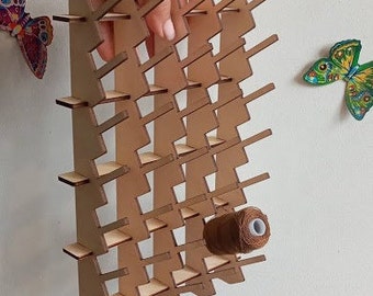 May include: A wooden thread rack with a zig-zag design. The rack is made of light brown wood and has 24 slots for holding spools of thread. A spool of brown thread is in one of the slots.