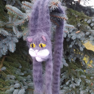May include: A gray and white knitted scarf with a cat face design. The cat has yellow eyes and a white nose and whiskers.