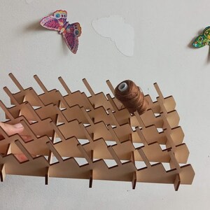 May include: A wooden thread rack with a brown spool of thread on top. The rack has a triangular shape and is made of light brown wood. It has multiple slots for holding spools of thread.