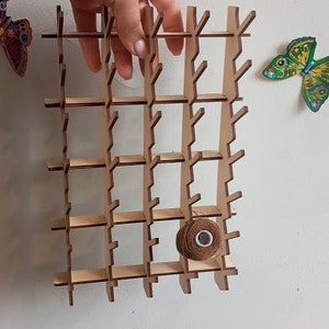 May include: A wooden wall-mounted organizer with a grid pattern and multiple compartments. A brown spool of thread is placed in one of the compartments.