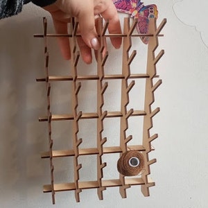 May include: Wooden thread rack with a grid of compartments for storing spools of thread. A single spool of brown thread is in one of the compartments.